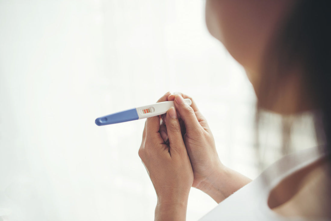 Femme tenant un test de grossesse positif, symbolisant la joie et l'espoir d'une future maternité.