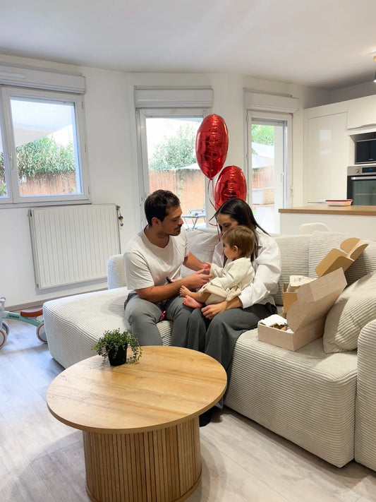 Jeunes parents souriants avec leur bébé sur un canapé, ambiance familiale chaleureuse.